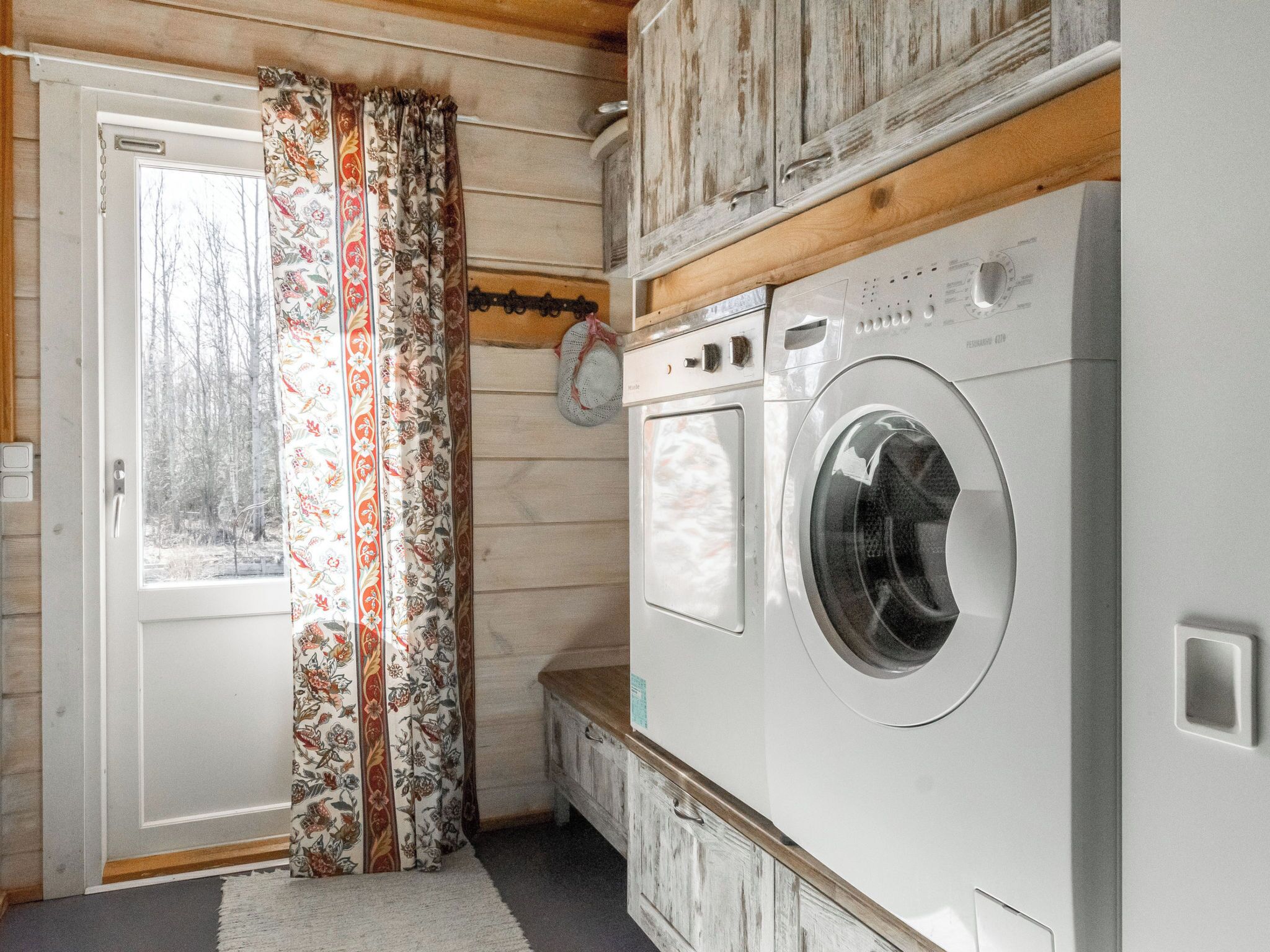 A laundry room with a washing machine, a door with a floral curtain, and wooden walls.