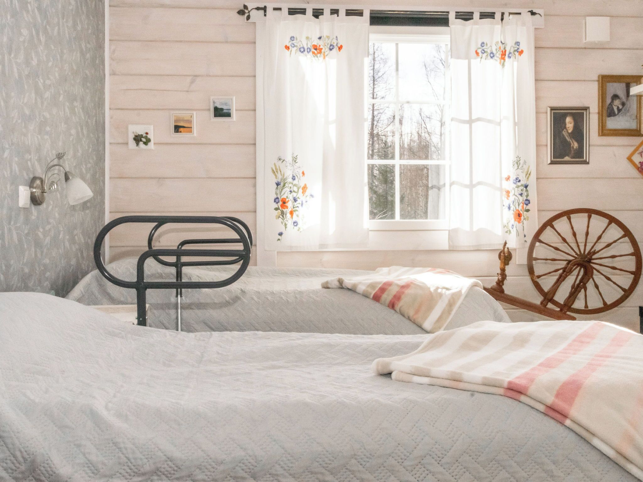 Een slaapkamer met een bed, een stoel, een raam met gordijnen, een wandklok en een fotolijst.