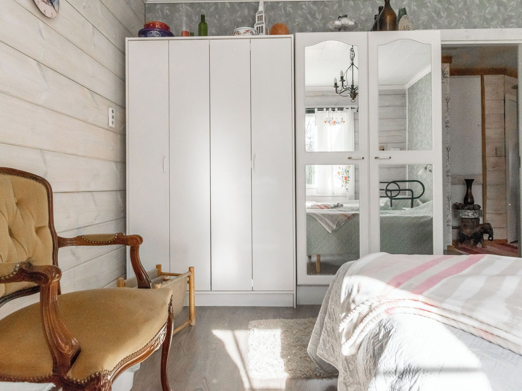 Un dormitorio con cama, una silla, un armario y un espejo.