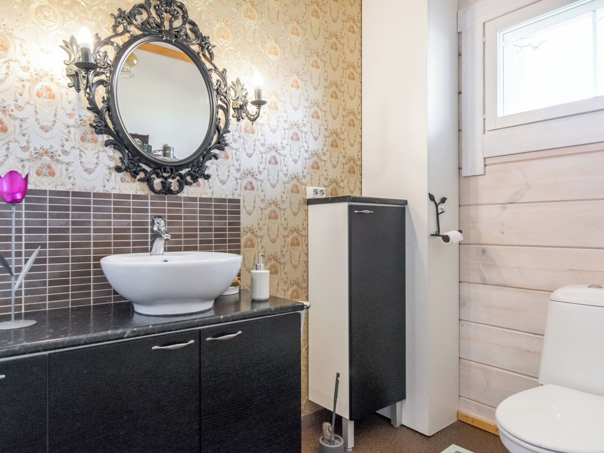 Un baño con lavamanos blanco, mueble negro y espejo con marco decorativo.