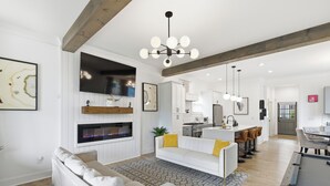 Una sala de estar moderna con chimenea, sofás blancos, un comedor y una cocina.