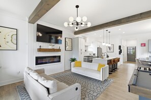 Ein modernes Wohnzimmer mit Kamin, weißen Sofas, einem Essbereich und einer Küche.