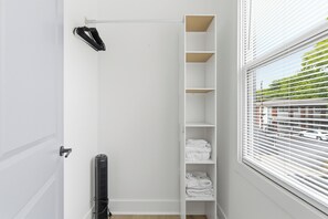 Ein weißer Kleiderschrank mit Regalen, einem Heizkörper und einem Fenster mit Jalousien.