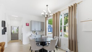 Una cocina moderna con armarios blancos, un comedor con mesa y sillas redondas, y un ventanal con cortinas.