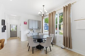 Eine moderne Küche mit weißen Schränken, einem Essbereich mit rundem Tisch und Stühlen sowie einem großen Fenster mit Vorhängen.