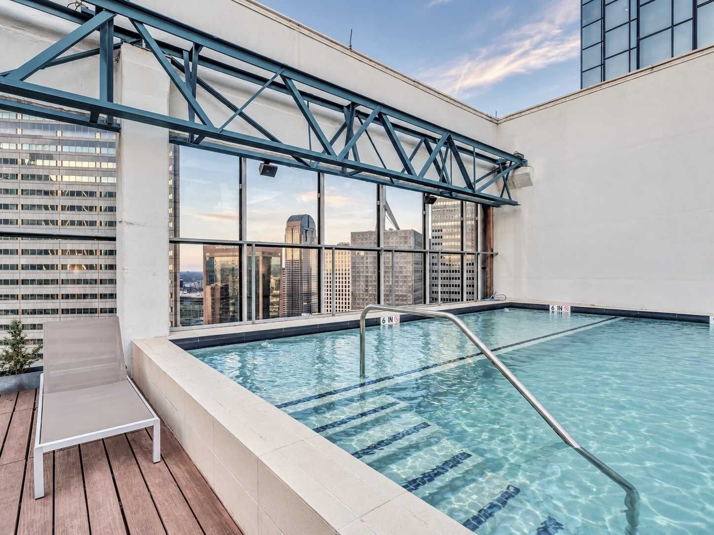 An indoor swimming pool with clear blue water, a wooden deck, and a view of city buildings.