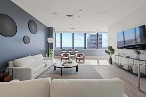 Un salon moderne avec un canapé, une table basse et des fauteuils, un grand téléviseur et une vue sur la ville.