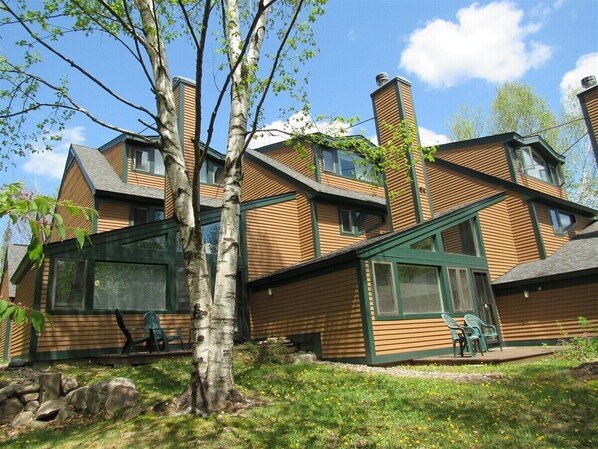 A wooden cabin with a sloped roof, large windows, and a small porch with chairs. - 3-bedroom townhome in wonderful Waterville Valley with AC (Waterville Valley)
