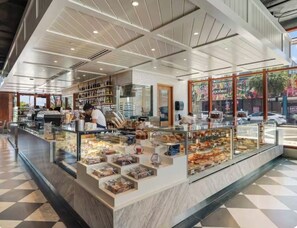 A bakery with a glass display case filled with pastries, a counter with baked goods, and a person working behind the counter. - New Studio in Wynwood (Miami)