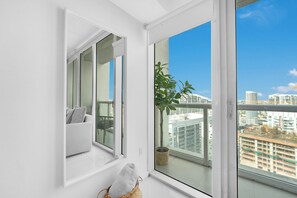 A balcony with a view of city buildings, a white wall, and a window with a plant. - 48th floor studio ★ Icon Brickell ★ (Miami)