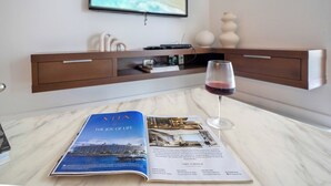 Eine Zeitschrift auf einem Tisch, ein Weinglas und ein Fernseher, der eine Strandansicht zeigt.