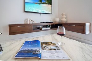 Eine Zeitschrift auf einem Tisch, ein Weinglas und ein Fernseher, der eine Strandansicht zeigt.