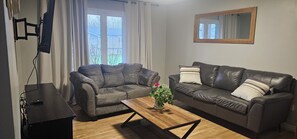 A living room with two sofas, a coffee table, and a TV mounted on the wall. - Pondview Gardens (Grand Falls-Windsor)