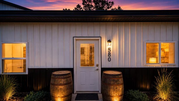 A building with a white exterior, a front door, and two barrels on either side.