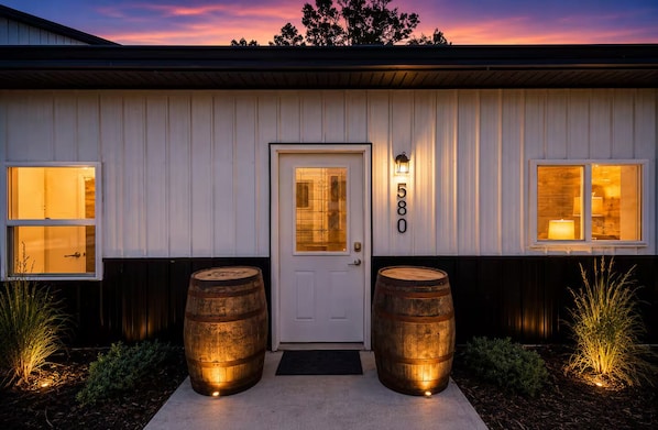 A building with a white exterior, a front door, and two barrels on either side.