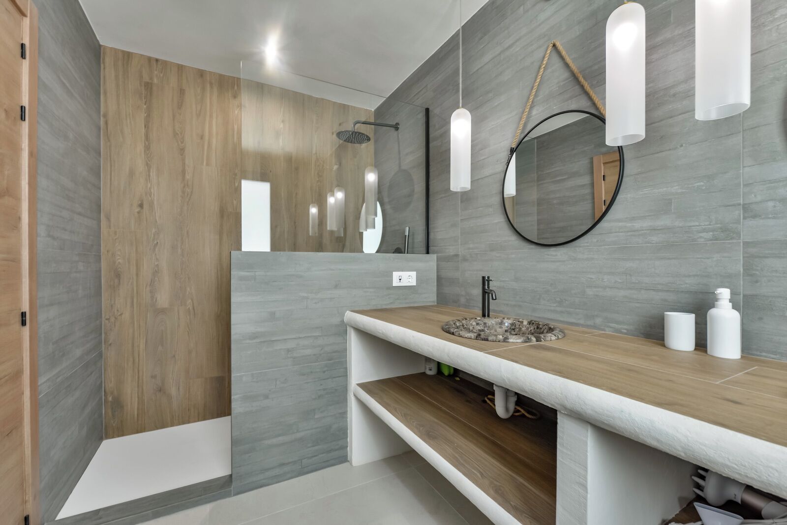 Une salle de bain moderne avec un meuble-lavabo en bois, un miroir rond et un espace douche.