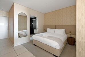 Ein modernes Hotelzimmer mit einem großen Bett, einem Spiegel, einem Kleiderschrank und einem kleinen Nachttisch.