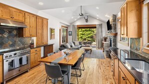 A kitchen with wooden cabinets, a stone backsplash, and a large dining table with chairs. - Heart of Suncadia: Fenced Yard, Hot Tub, BBQ, EV Charge, (Cle Elum)