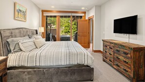 A bedroom with a large bed, a dresser, a television, and a sliding glass door leading to a patio. - Heart of Suncadia: Fenced Yard, Hot Tub, BBQ, EV Charge, (Cle Elum)