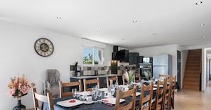 Una cocina moderna con zona de comedor, sillas de madera, un reloj y una escalera.