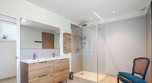 Un baño moderno con ducha envuelta en vidrio, tocador de madera y una silla.