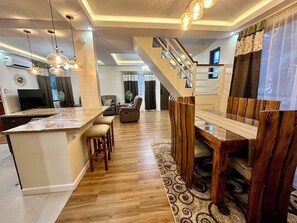 A modern kitchen with a central island, wooden dining table, and a staircase leading to an upper level. - BethShalom Guest House by Jeff and Malou, 4 Bedrooms and 2 Bathrooms (Dasmarinas)