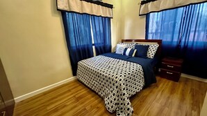 A bedroom with a bed, curtains, a nightstand, and an air conditioning unit. - BethShalom Guest House by Jeff and Malou, 4 Bedrooms and 2 Bathrooms (Dasmarinas)