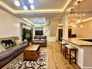 A modern living room with a sofa, coffee table, and a dining area with bar stools. - BethShalom Guest House by Jeff and Malou, 4 Bedrooms and 2 Bathrooms (Dasmarinas)