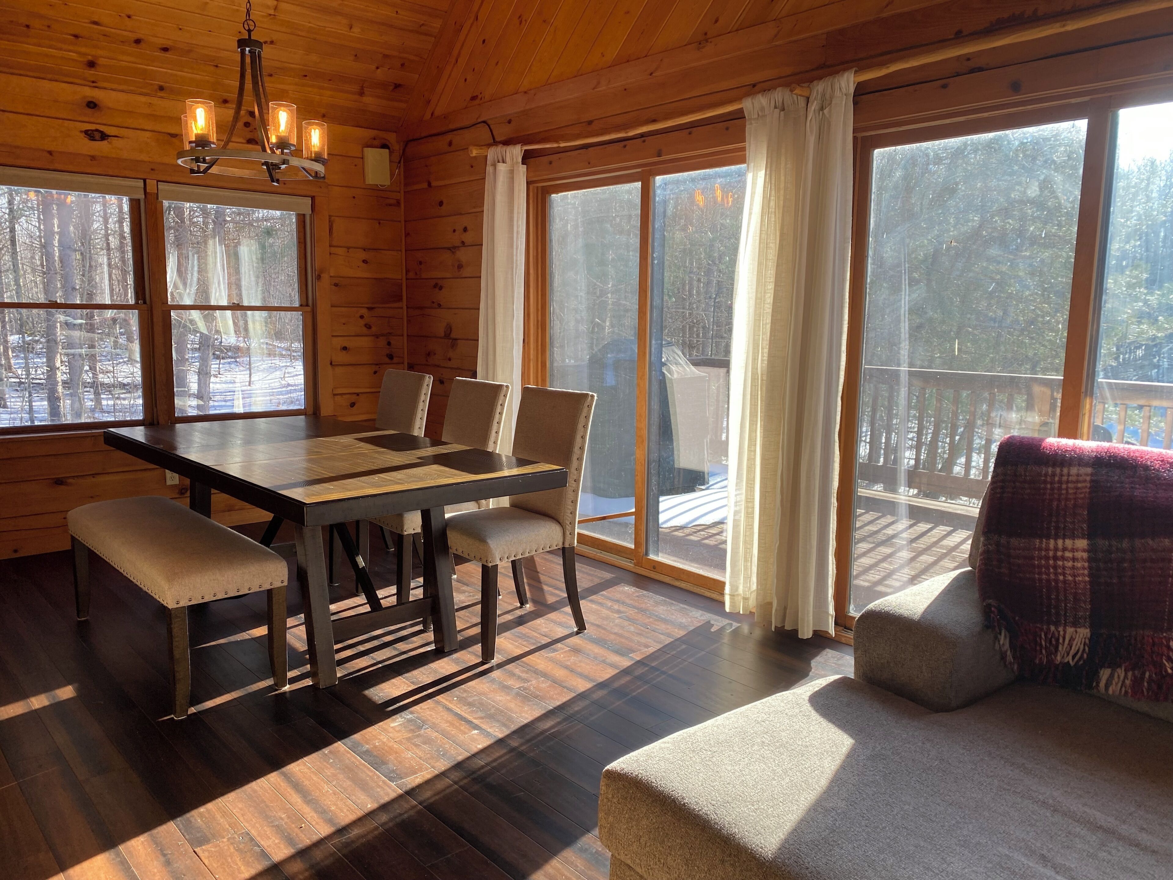 L’intérieur d’un chalet en bois comprend une table à manger, des chaises, un banc et de grandes fenêtres qui offrent une vue sur un paysage enneigé.