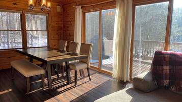L’intérieur d’un chalet en bois comprend une table à manger, des chaises, un banc et de grandes fenêtres qui offrent une vue sur un paysage enneigé.