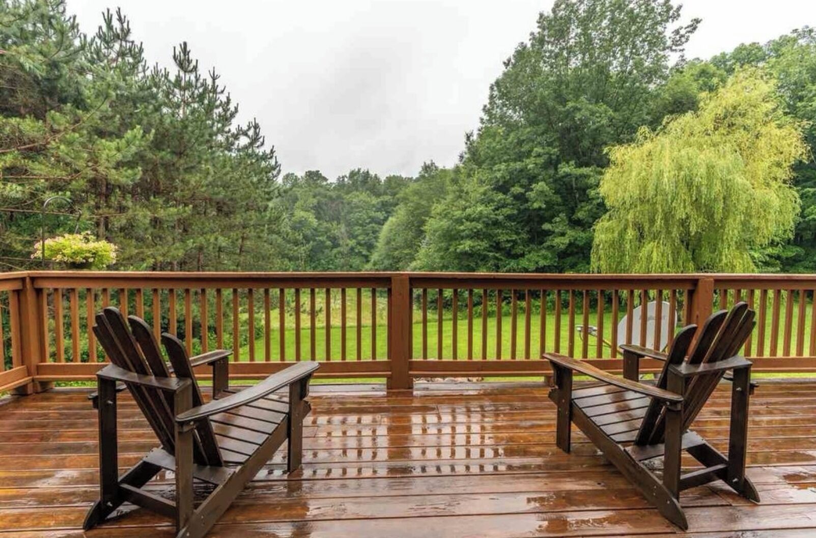 A wooden deck with two chairs and a table, overlooking a grassy area with trees.