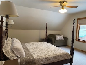 A bedroom with a four-poster bed, a ceiling fan, a window with a view, and a small table.