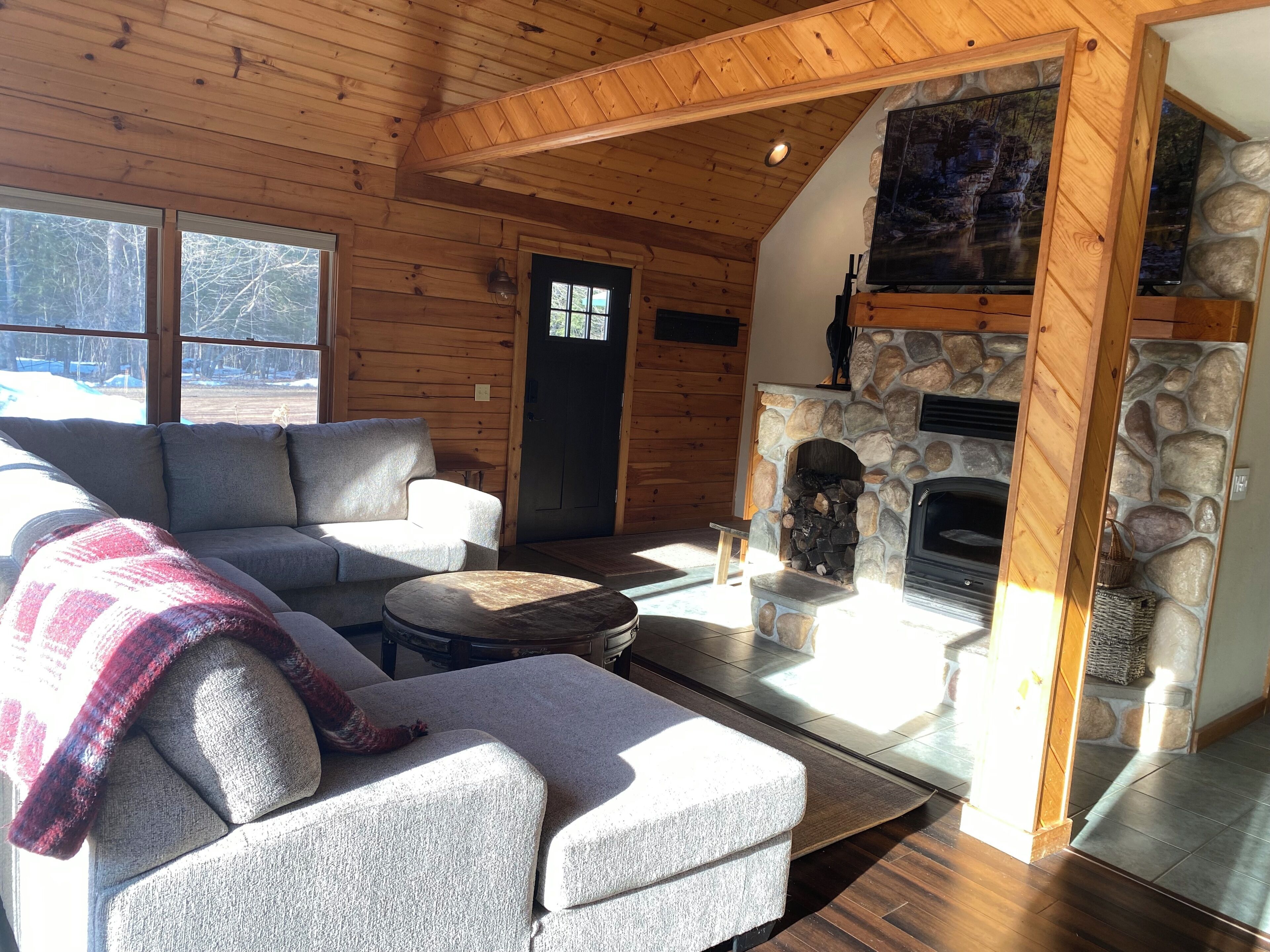 A cozy cabin interior with a stone fireplace, wooden walls, and a sofa.