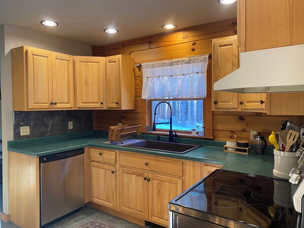 A kitchen with wooden cabinets, a black stove, and a window with a view of a snowy landscape.