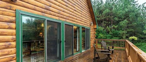 A log cabin with a wooden deck and a chair.