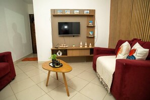 Ein Wohnzimmer mit Fernseher, einem roten Sofa, einem Holztisch und Regalen mit Dekoration.