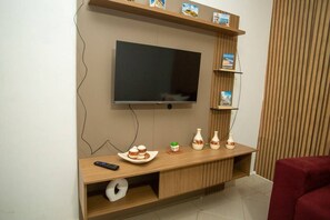 Ein modernes Wohnzimmer mit einem Flachbildfernseher an einer Holzwand, einer Holzunterhaltungsecke darunter und einem roten Sofa.