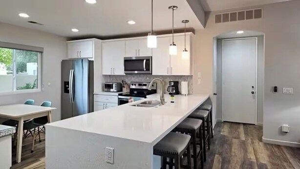 A modern kitchen with white cabinets, stainless steel appliances, pendant lighting, and a bar area with stools. - Palm Springs Oasis w/Pool & Golf Access (Cathedral City)