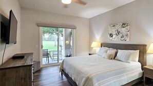 A bedroom with a large bed, a TV, a sliding glass door to a patio, and a painting on the wall. - Palm Springs Oasis w/Pool & Golf Access (Cathedral City)