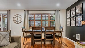 A dining area with a wooden table and chairs, a large wall clock, and a window with blinds. - Mt Hood Cabin: River, Trails, Pool, Dog-Friendly (Rhododendron)