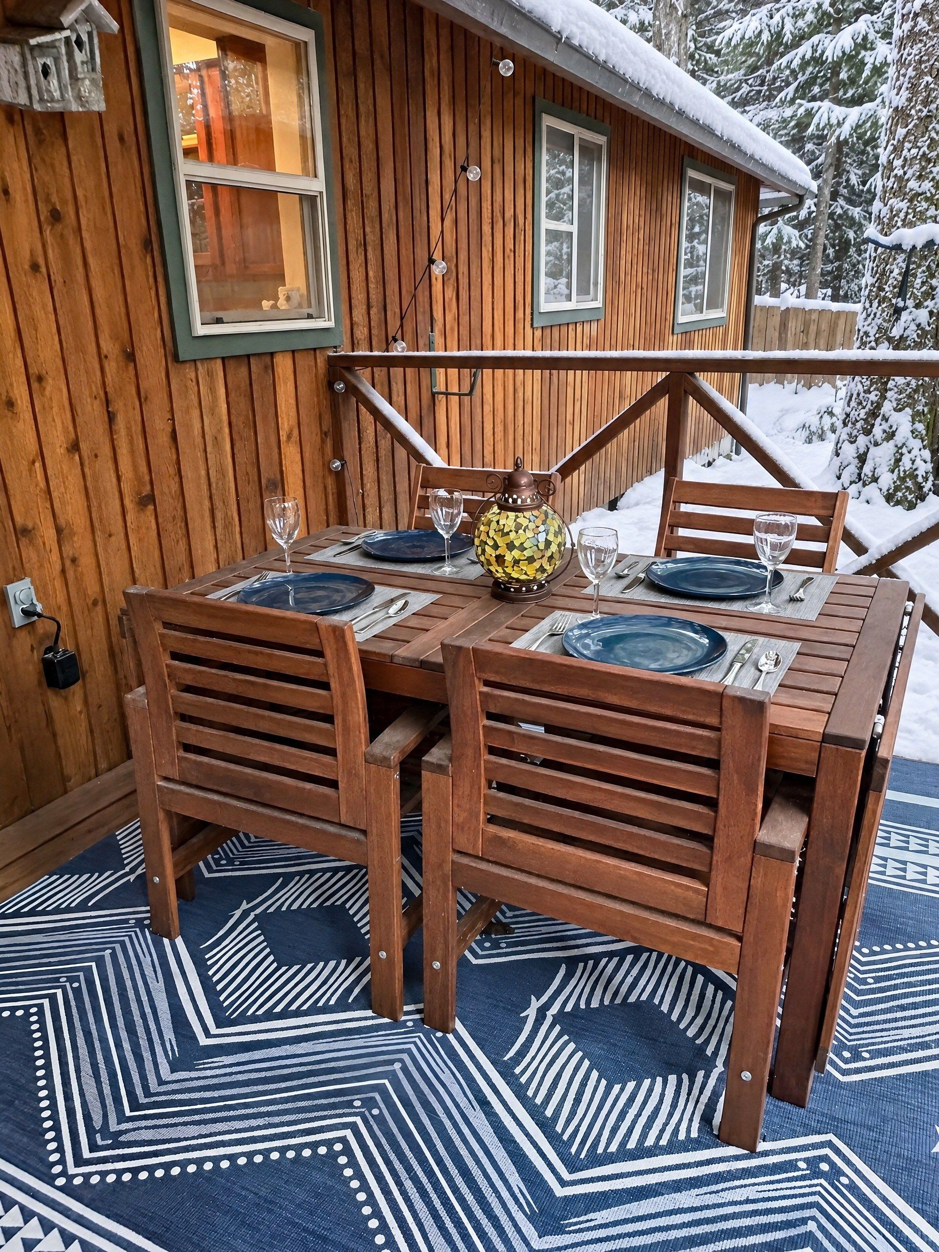 A wooden dining table with chairs, a patterned rug, and a snow-covered exterior.