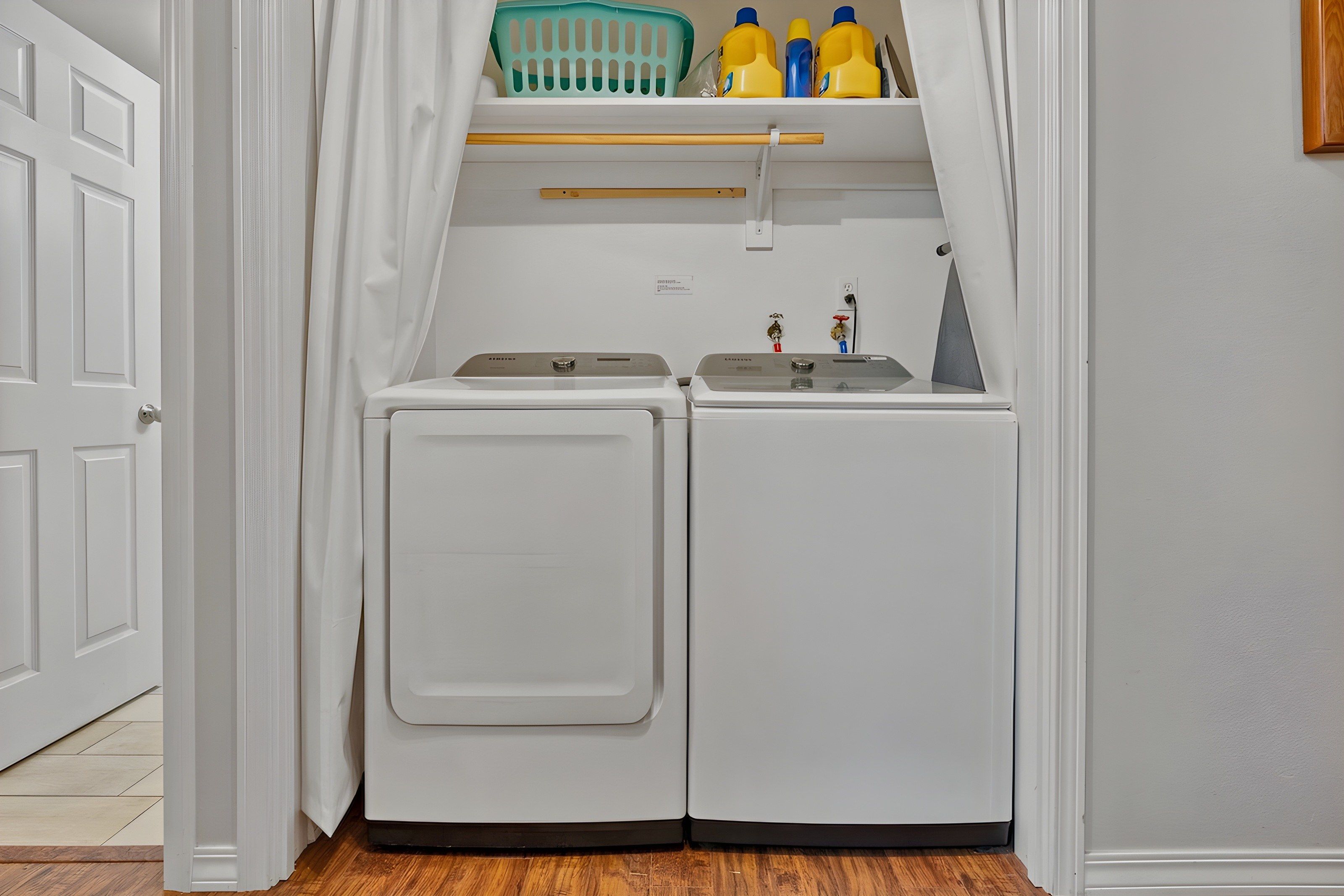 A laundry room with two front-loading washing machines, a shelf with laundry detergent bottles, and a small shelf above the machines.