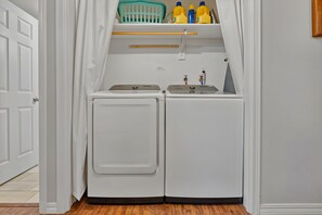 A laundry room with two front-loading washing machines, a shelf with laundry detergent bottles, and a small shelf above the machines. - Family Winter Cabin • Game Room • Dogs OK (Rhododendron)
