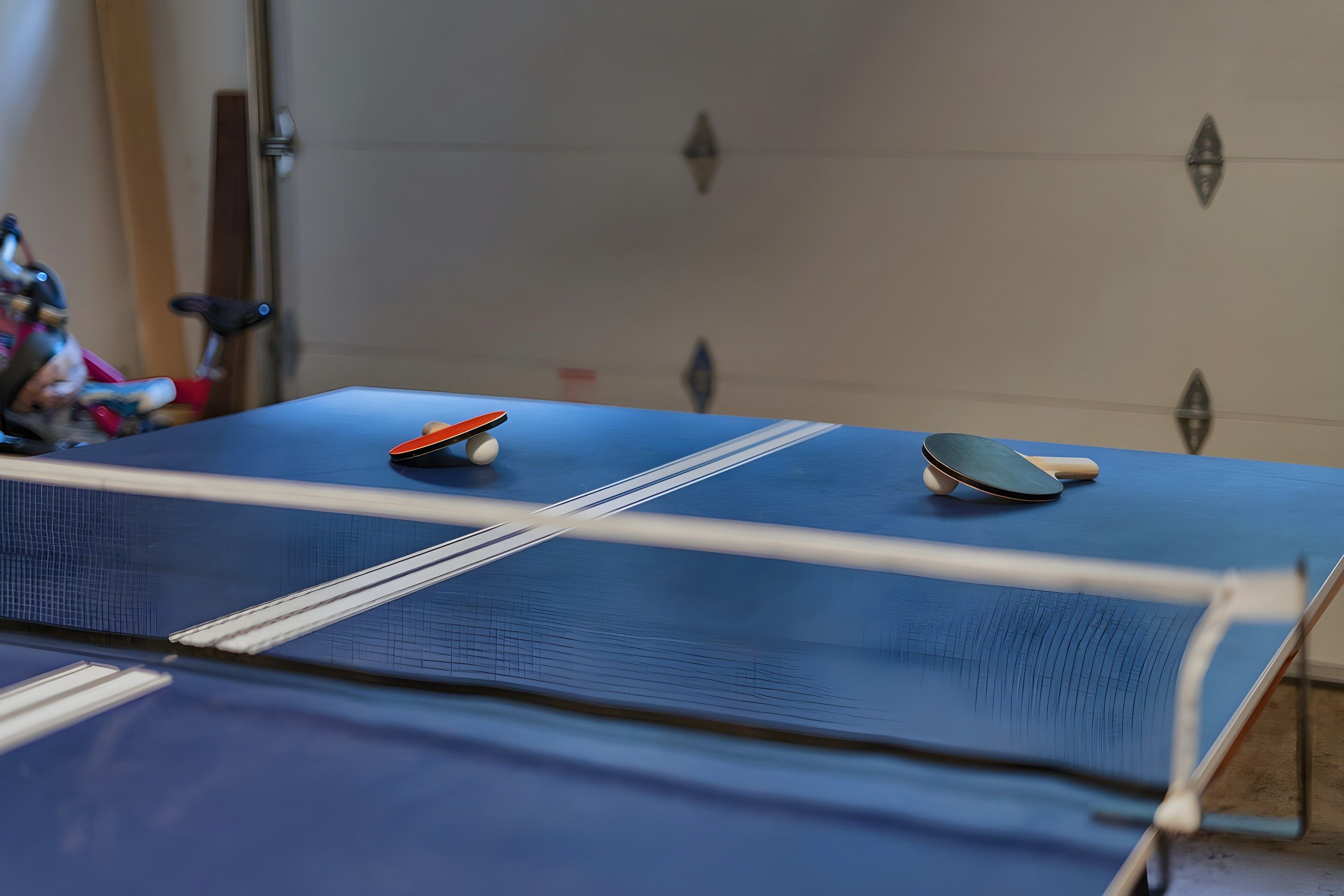 Une table de ping-pong avec deux raquettes et une balle, placée devant un mur uni.