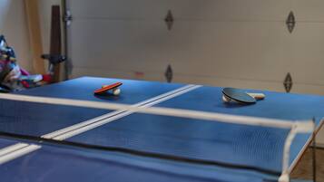 A ping pong table with two paddles and a ball, set against a plain wall.