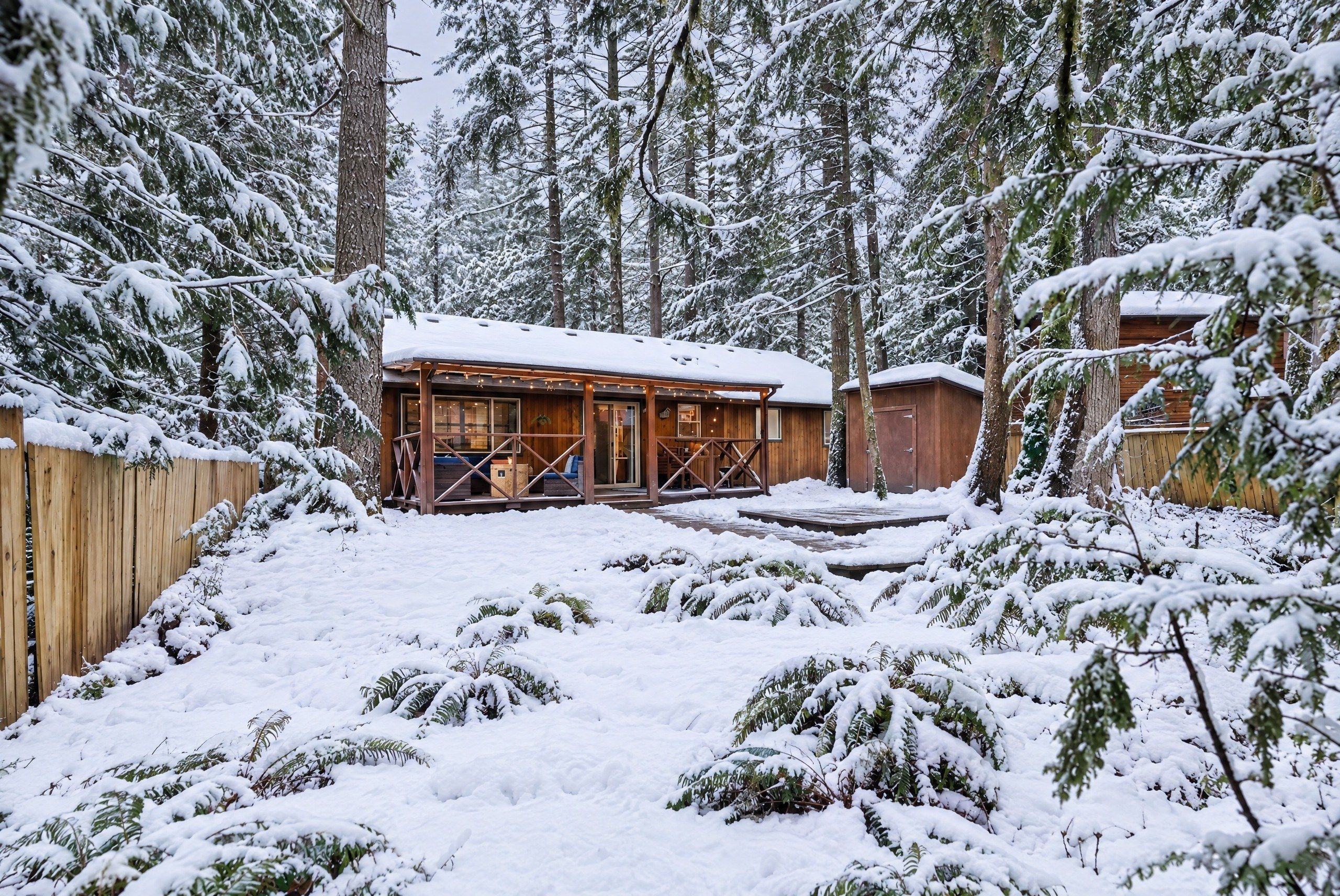 Eine Hütte mit Veranda und einer Terrasse, umgeben von schneebedeckten Bäumen.