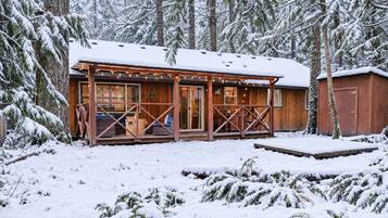 A wooden cabin with a covered porch, surrounded by snow-covered trees.