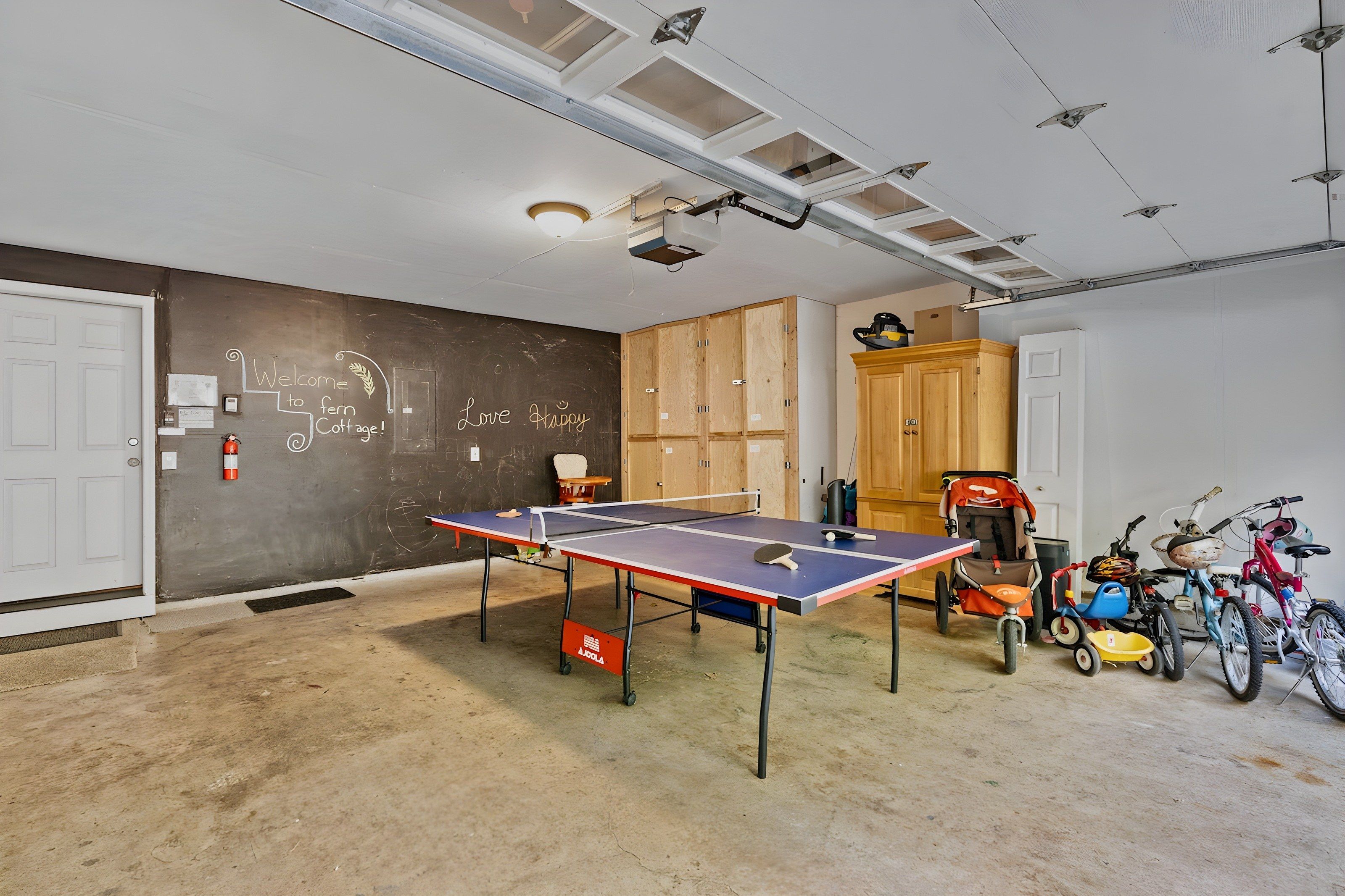 A room with a ping pong table, wooden cabinets, and bicycles.