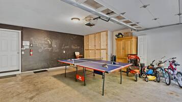A room with a ping pong table, wooden cabinets, and bicycles.