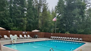 A swimming pool with a wooden deck, lounge chairs, and a flag. - Mt Hood Cabin: River, Trails, Pool, Dog-Friendly (Rhododendron)